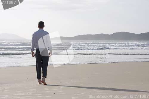 Image of Businessman walking barefoot on a beach