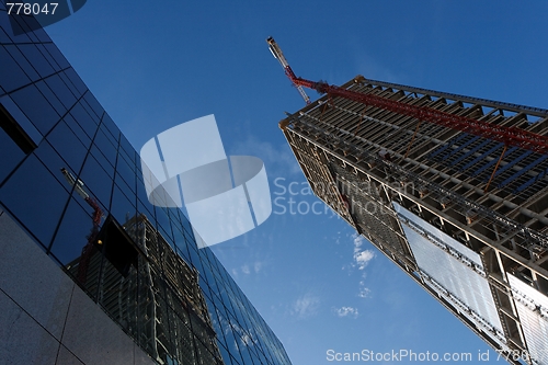 Image of Lifting crane and high building under construction reflecting in another building