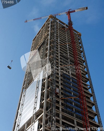 Image of Lifting crane hoisting a weight at skyscraper construction site