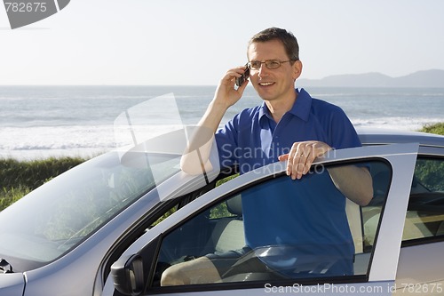 Image of Man talking on cell phone beside a car at the sea