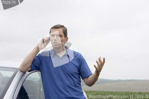 Image of Angry man talking on cell phone beside a car