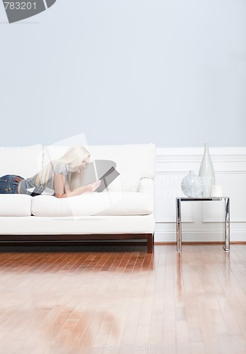 Image of Young Woman Lying on Sofa Reading Book