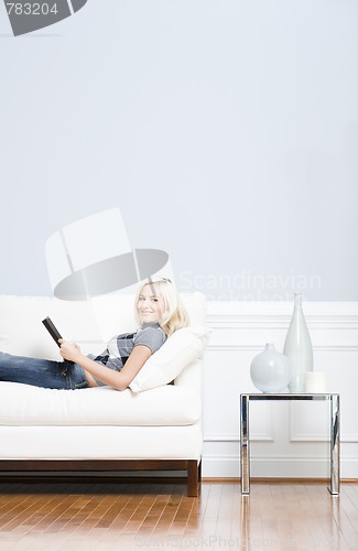 Image of Young Woman Lying on Sofa Reading Book