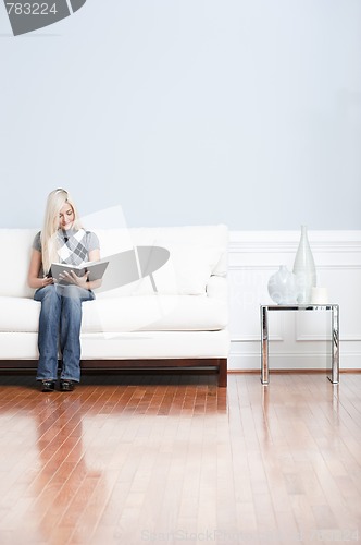 Image of Young Woman Sitting on Sofa Reading Book