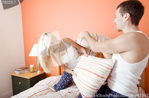 Image of Young Couple Kneeling on Bed Having a Pillow Fight