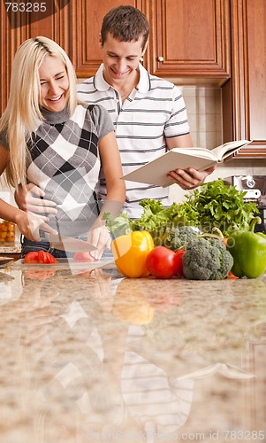 Image of Young Man Holding Book Next to Woman Cutting Tomato