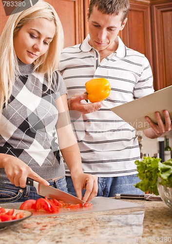 Image of Young Man Holding Book Next to Woman Cutting Tomato