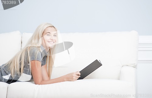 Image of Smiling Woman Reclining on Couch With Book