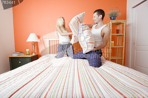 Image of Young Couple Kneeling on Bed Having a Pillow Fight