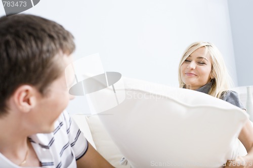 Image of Young Woman Smiling and Hitting Young Man With Pillow