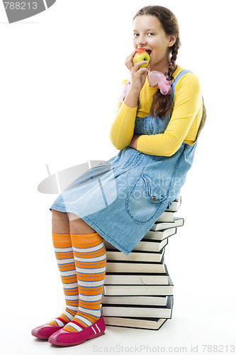 Image of  girl sit on pile of books and eat apple