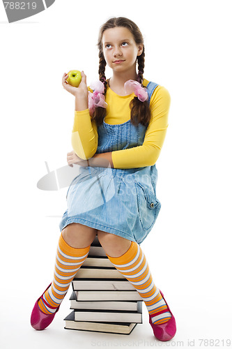 Image of Girl eat apple sitting on pile of books