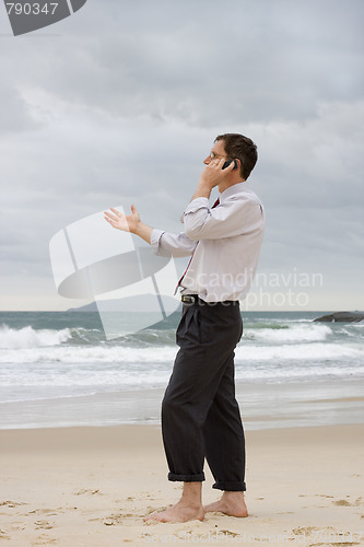 Image of Businessman talking on cell phone on a beach