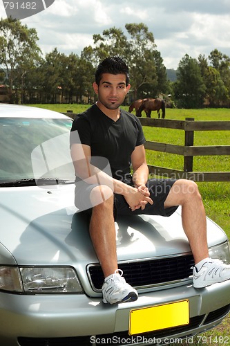 Image of Man sitting on bonnet of silver car in countryside