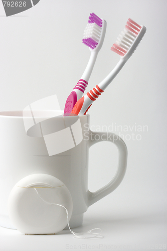 Image of Two toothbrushes in a cup and dental floss