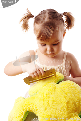 Image of Cute girl combing her soft toy