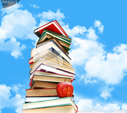 Image of Pile of books and apple against blue sky