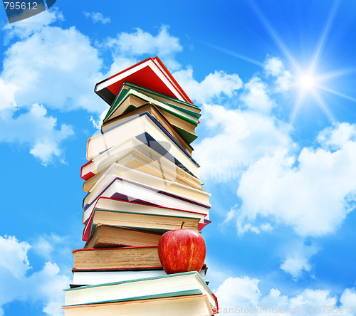 Image of Pile of books and apple against blue sky