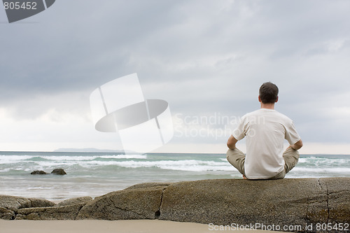 Image of Man meditating on a rock at the sea