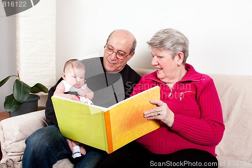 Image of Grandparents reading book to baby girl.