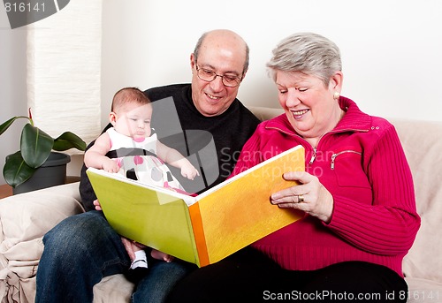 Image of Grandparents reading book to baby girl.