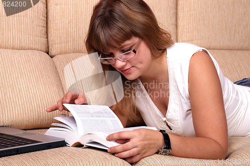 Image of  Beautiful student girl lying on the sofa with book and laptop.