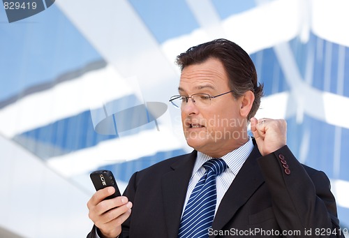 Image of Businessman Looking at Cell Phone Clinches His Fist in Joy