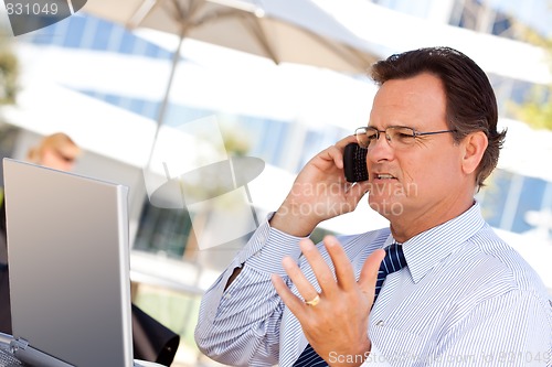 Image of Businessman Talking on Cell Phone Using Laptop