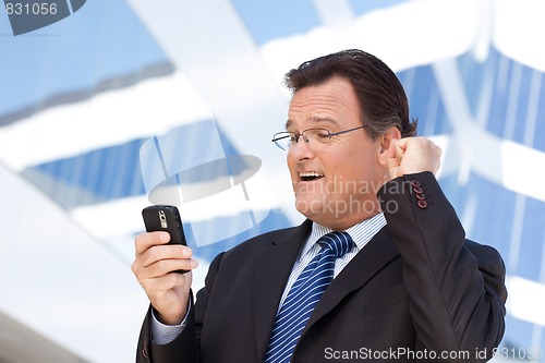 Image of Businessman Looking at Cell Phone Clinches His Fist in Joy