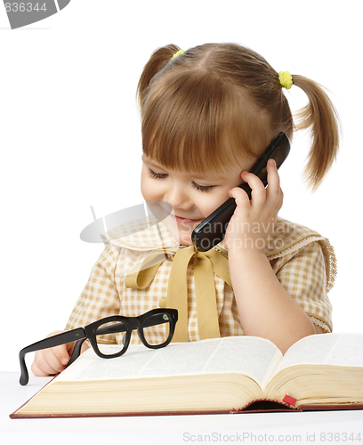 Image of Cute little girl with book talking to a cell phone