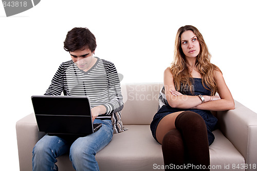 Image of couple sitting on the couch, he playing computer and she look to other way bored