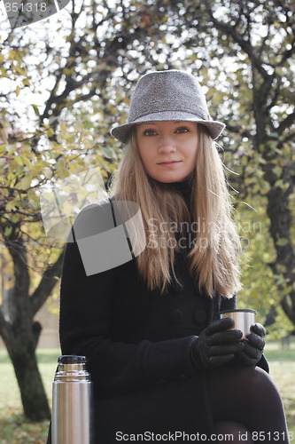 Image of Woman in black coat and hat with cup