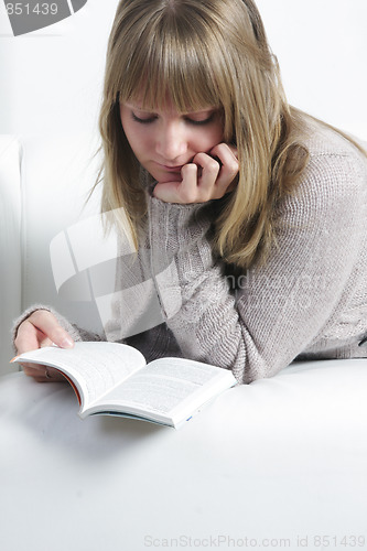 Image of Woman reading book laying on sofa