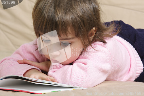 Image of Little girl reading book on sofa
