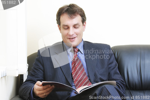 Image of Smiling businessman reading magazine