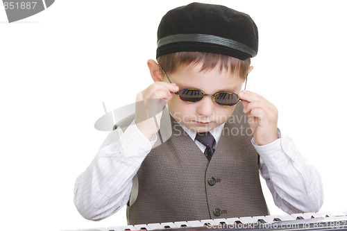 Image of Cute kid adjusting spectacles at piano keyboard