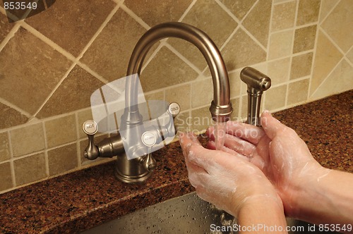 Image of Soapy hand washing under flowing water out of a faucet