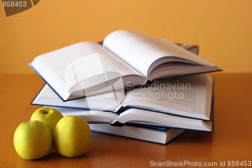 Image of three green apples and four opened books on the desk