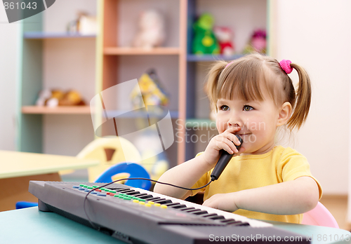 Image of Girl play on a piano and sing in microphone