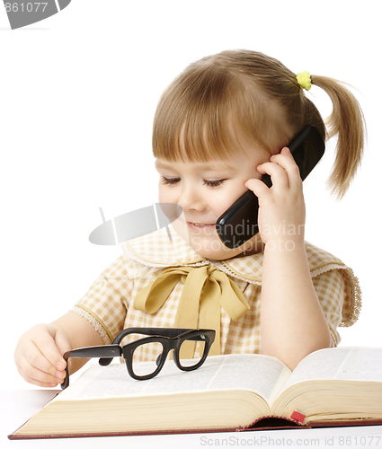 Image of Cute little girl with book talking to a cell phone