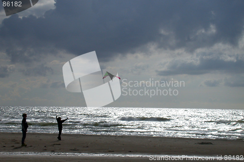 Image of To børn leger på stranden med drage