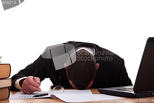 Image of Stressed young man sitting at a table among books and laptop