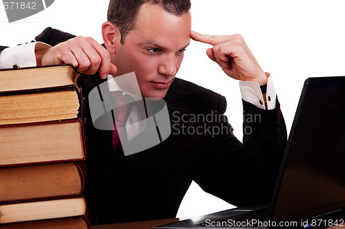 Image of businessman on desk with books, looking at the computer