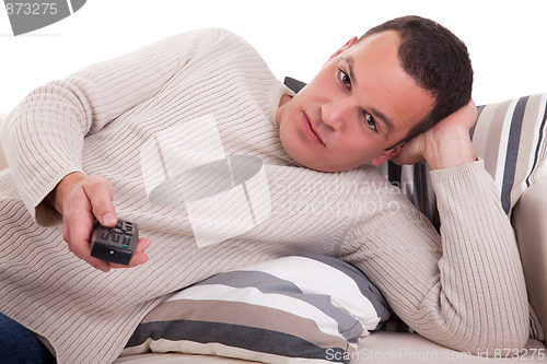 Image of casual man, lying on the couch, watching television with the command at hand