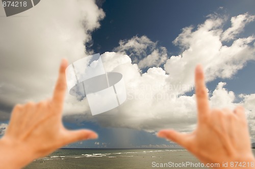 Image of Hands Framing Dramatic Clouds over Tropical Shoreline