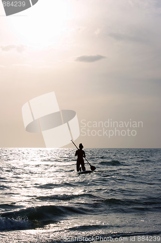 Image of woman paddleboarding towards sun