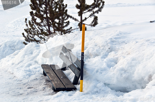 Image of Snow covered bench and snow pole