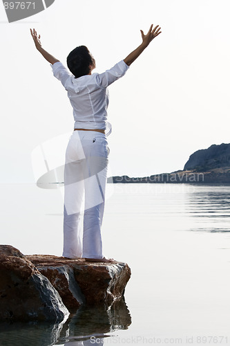 Image of Young woman meets sunrise staying barefoot on the sea stone