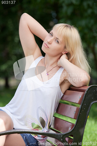 Image of Pretty  blond woman sits with raised arms on park bench