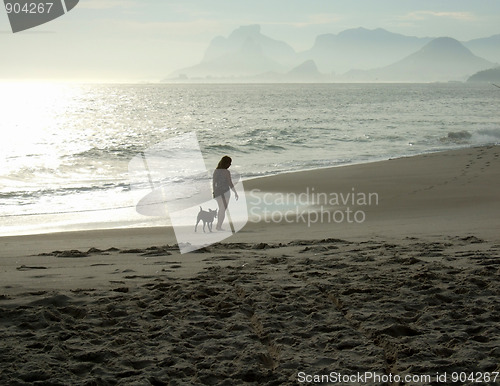 Image of Woman walking with her dog on the beach sand